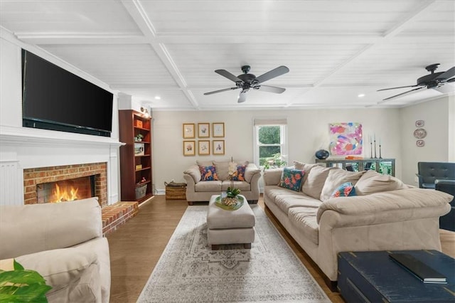 living room with dark wood-type flooring, coffered ceiling, a brick fireplace, ceiling fan, and beam ceiling