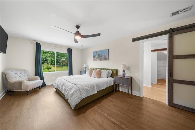 bedroom with wood-type flooring, a barn door, and ceiling fan