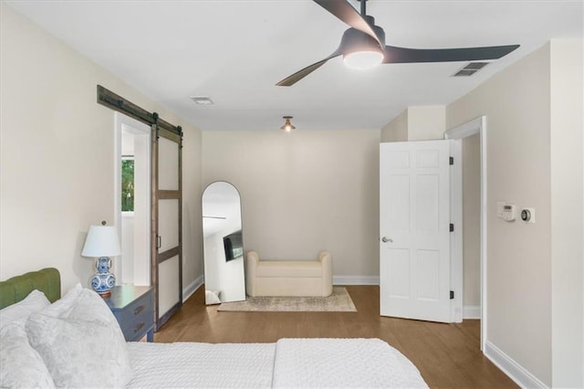 bedroom featuring dark hardwood / wood-style flooring, a barn door, and ceiling fan