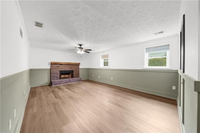 unfurnished living room with plenty of natural light, a textured ceiling, a brick fireplace, and light wood-type flooring