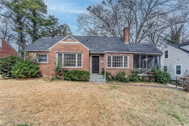 view of front facade featuring brick siding, a chimney, a front lawn, and a sunroom