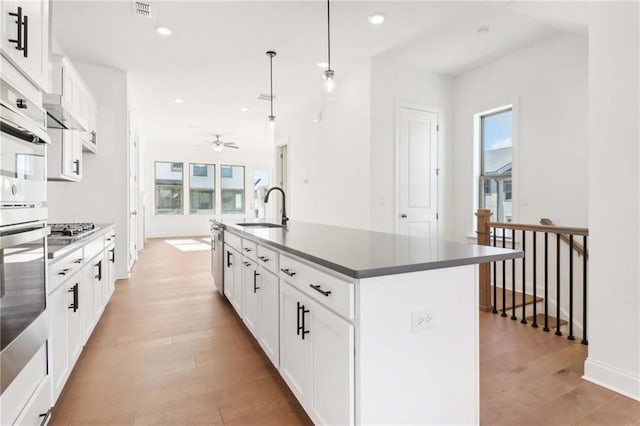 kitchen featuring hanging light fixtures, a wealth of natural light, white cabinetry, and a kitchen island with sink