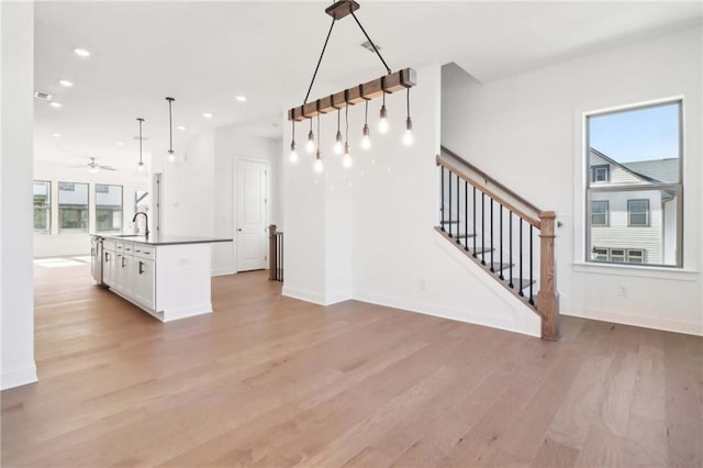 kitchen featuring white cabinetry, sink, hanging light fixtures, light hardwood / wood-style floors, and a kitchen island with sink