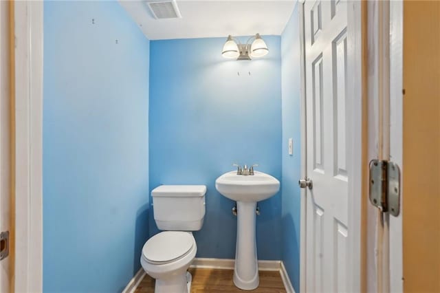 half bath featuring toilet, wood finished floors, visible vents, and baseboards