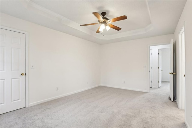 empty room featuring a tray ceiling, baseboards, light colored carpet, and ceiling fan