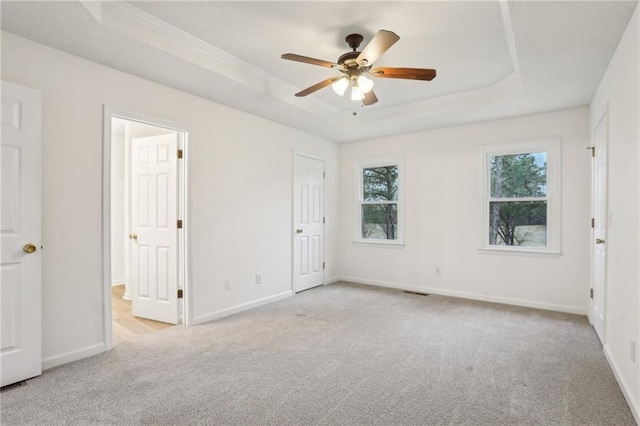 unfurnished bedroom with carpet flooring, a ceiling fan, a raised ceiling, and baseboards