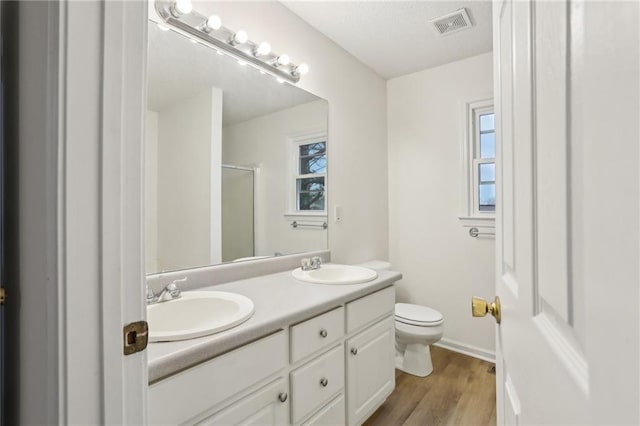 full bath with visible vents, toilet, double vanity, a stall shower, and a sink