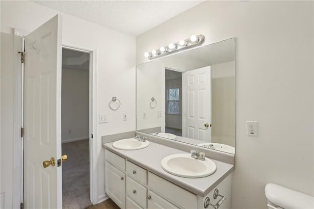 full bath with a textured ceiling, double vanity, toilet, and a sink