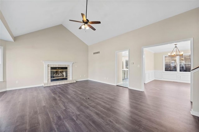 unfurnished living room featuring a tiled fireplace, high vaulted ceiling, dark wood-type flooring, and ceiling fan with notable chandelier