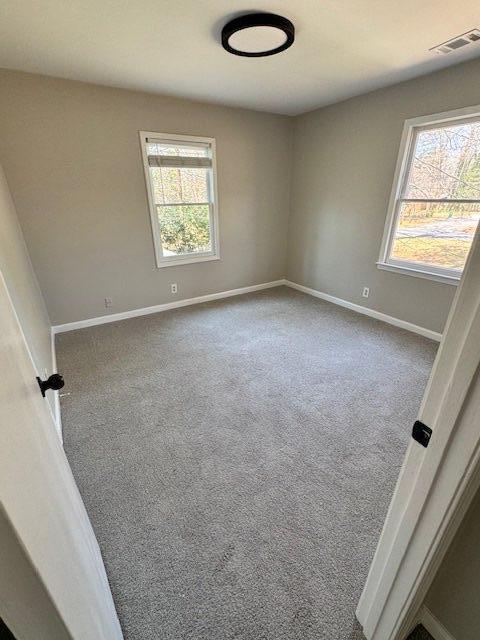 unfurnished room with carpet flooring, baseboards, visible vents, and plenty of natural light