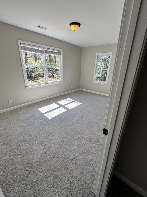 carpeted spare room featuring visible vents, baseboards, and a healthy amount of sunlight