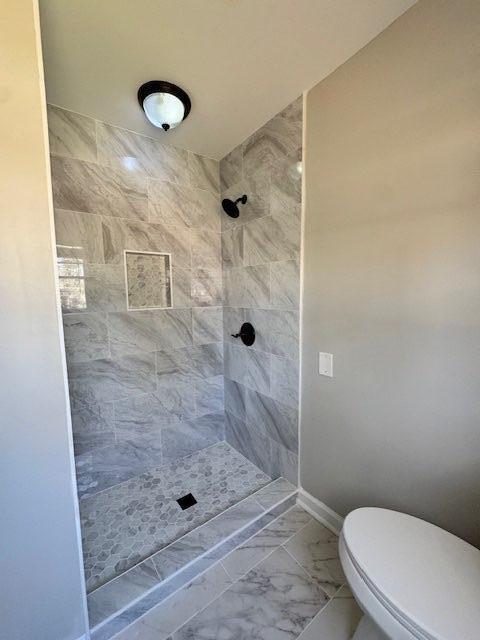 bathroom with baseboards, toilet, marble finish floor, and a tile shower