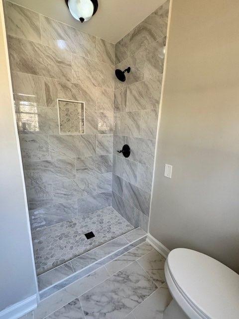 bathroom with toilet, baseboards, marble finish floor, and a tile shower