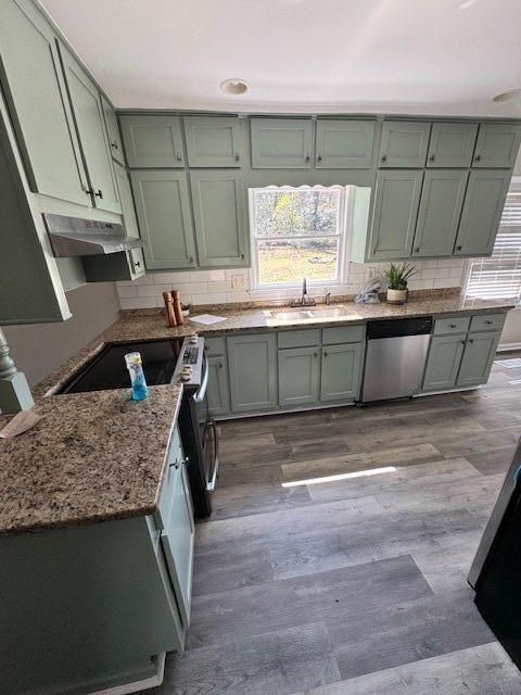 kitchen with backsplash, light stone countertops, under cabinet range hood, appliances with stainless steel finishes, and a sink