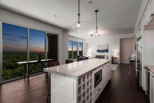 kitchen featuring stainless steel microwave, decorative light fixtures, dark hardwood / wood-style flooring, white cabinets, and a center island