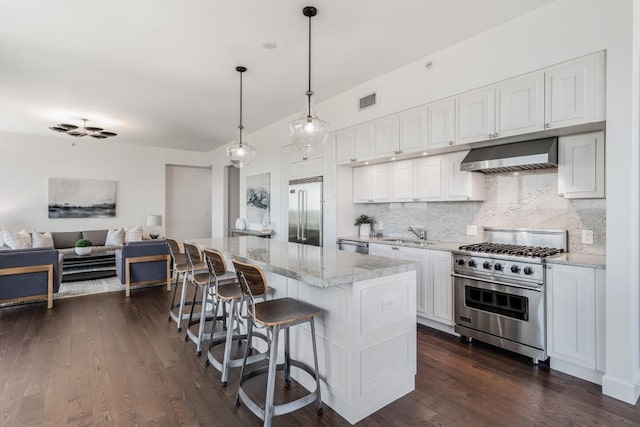 kitchen featuring white cabinets, a kitchen island, wall chimney range hood, backsplash, and high quality appliances