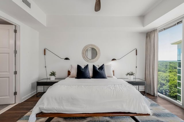 bedroom with a tray ceiling, multiple windows, dark hardwood / wood-style floors, and ceiling fan