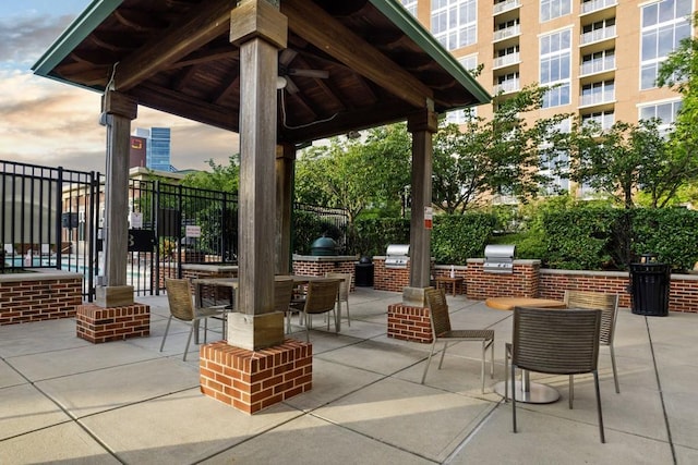 patio terrace at dusk with ceiling fan, a gazebo, exterior kitchen, and a grill