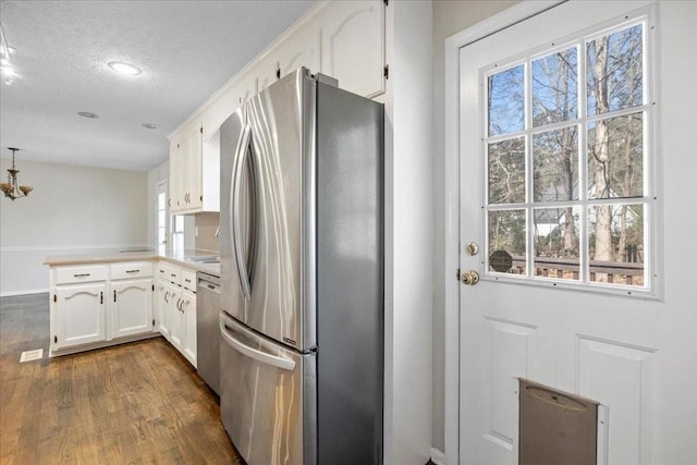 kitchen with a peninsula, dark wood-style flooring, white cabinets, appliances with stainless steel finishes, and a textured ceiling