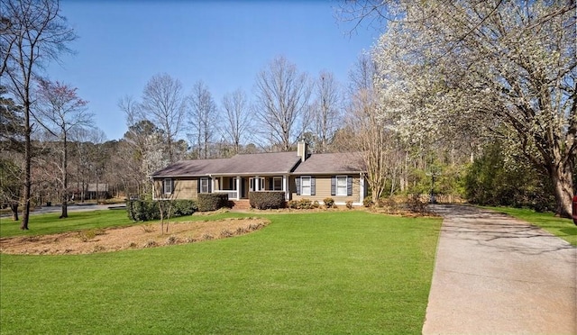 ranch-style home with driveway, a chimney, and a front yard