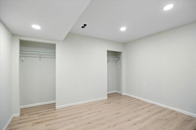 unfurnished bedroom featuring recessed lighting, two closets, baseboards, and wood finished floors