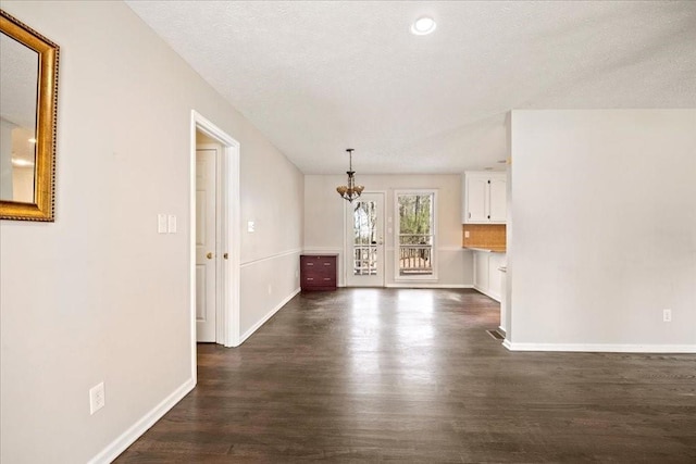 unfurnished living room with a chandelier, a textured ceiling, baseboards, and dark wood-style flooring