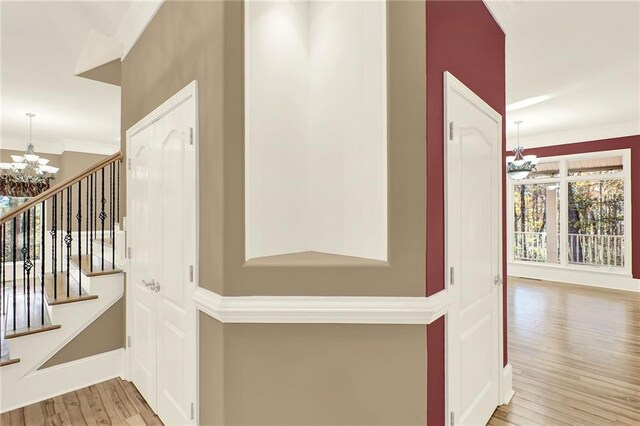 corridor with ornamental molding, light hardwood / wood-style floors, and an inviting chandelier