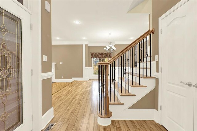 stairway with a chandelier, hardwood / wood-style floors, and ornamental molding