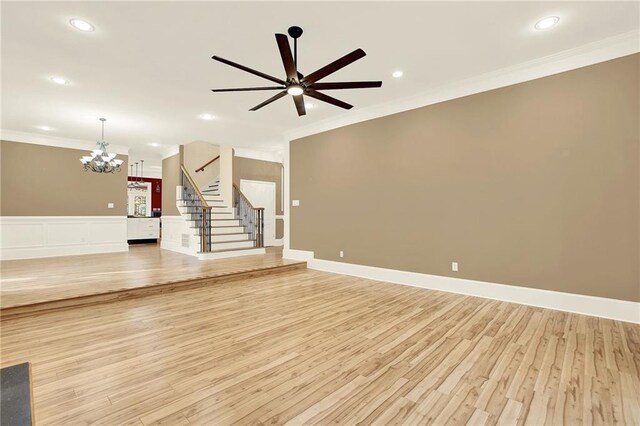 unfurnished living room with light hardwood / wood-style floors, ceiling fan with notable chandelier, and ornamental molding