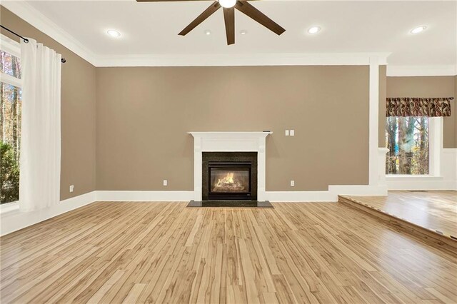 unfurnished living room featuring light wood-type flooring, a wealth of natural light, crown molding, and ceiling fan