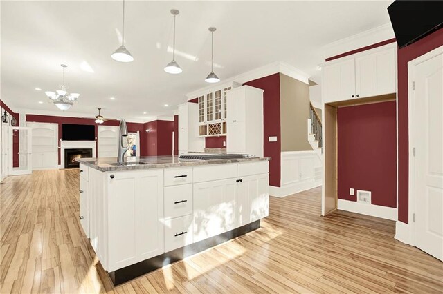 kitchen featuring white cabinets, light hardwood / wood-style flooring, hanging light fixtures, and an island with sink