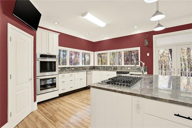 kitchen with light hardwood / wood-style flooring, white cabinets, decorative light fixtures, and appliances with stainless steel finishes