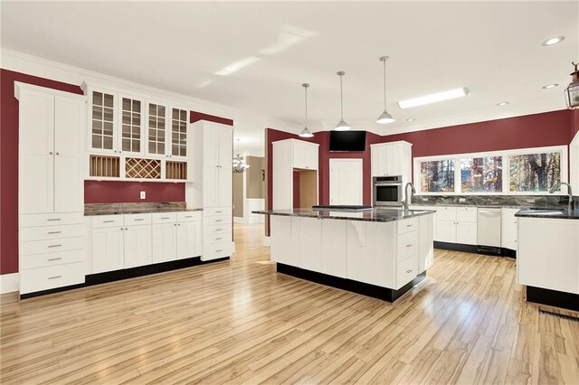 kitchen with appliances with stainless steel finishes, a kitchen island with sink, pendant lighting, light hardwood / wood-style flooring, and white cabinetry