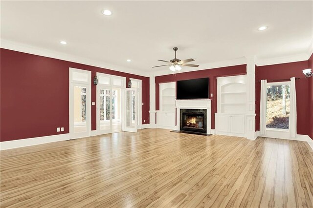 unfurnished living room featuring built in shelves, ceiling fan, and light hardwood / wood-style flooring