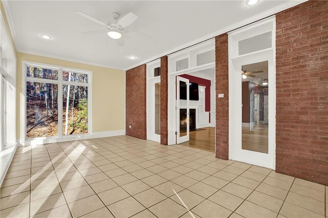 tiled spare room with ceiling fan, ornamental molding, a fireplace, and brick wall