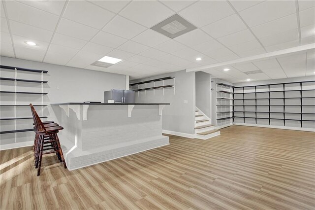 bar with a drop ceiling, light hardwood / wood-style floors, and stainless steel refrigerator