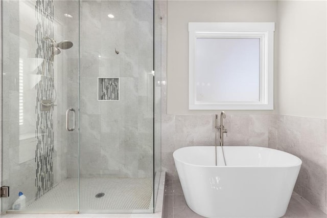 full bathroom featuring tile walls, a freestanding tub, and a stall shower