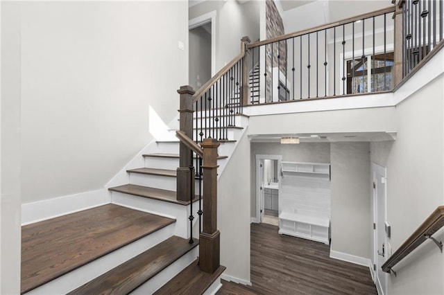 stairs with wood finished floors, baseboards, and a towering ceiling