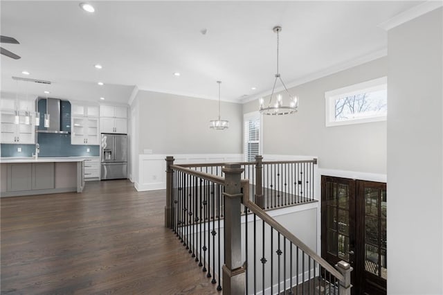 corridor with an upstairs landing, ornamental molding, a sink, a chandelier, and dark wood-style flooring