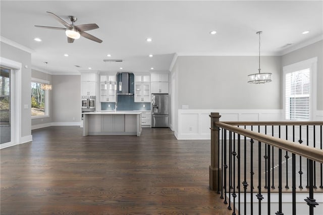 kitchen with white cabinetry, stainless steel appliances, crown molding, and wall chimney range hood