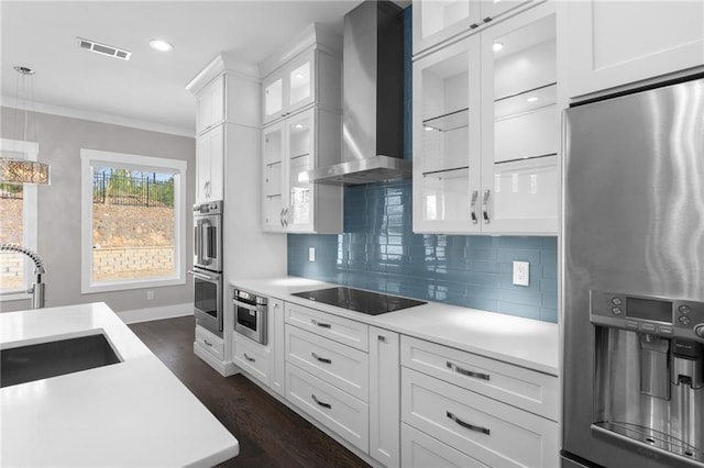 kitchen featuring a sink, ornamental molding, light countertops, stainless steel appliances, and wall chimney range hood