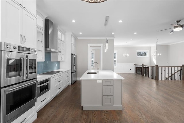 kitchen featuring a center island with sink, dark wood finished floors, a sink, stainless steel appliances, and wall chimney range hood