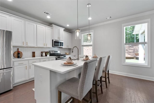 kitchen with white cabinetry, appliances with stainless steel finishes, a kitchen island with sink, pendant lighting, and dark hardwood / wood-style flooring