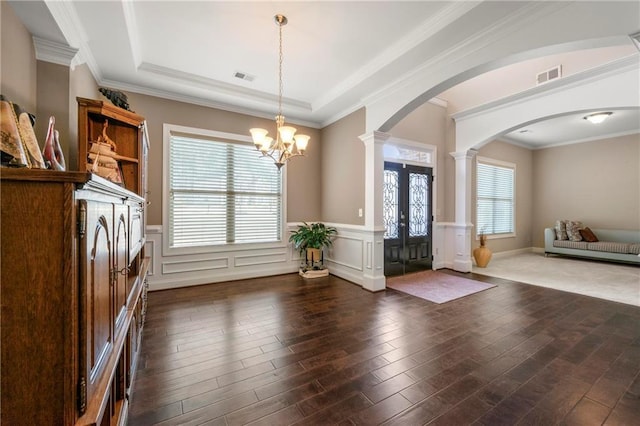 entryway with a tray ceiling, dark wood-type flooring, decorative columns, and a chandelier