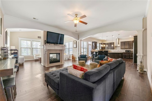 living room featuring crown molding, dark wood-type flooring, ceiling fan, and a multi sided fireplace