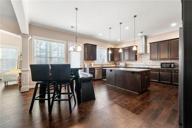 kitchen featuring wall chimney exhaust hood, dark brown cabinets, hanging light fixtures, stainless steel dishwasher, and a kitchen island