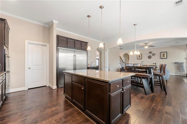 kitchen featuring built in fridge, a kitchen island, hanging light fixtures, light stone countertops, and dark brown cabinets