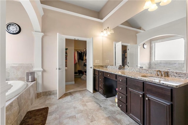 bathroom with vanity, decorative columns, and tiled bath