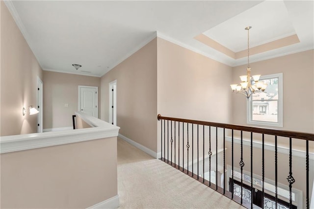 hall featuring crown molding, a tray ceiling, an inviting chandelier, and light carpet