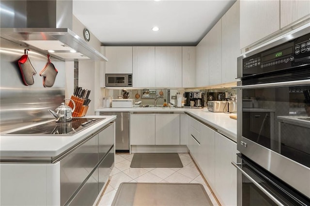 kitchen featuring light tile patterned floors, wall chimney exhaust hood, stainless steel microwave, light countertops, and black electric cooktop